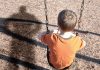 A young boy sitting on a swing at a playground, with his shadow cast on the ground