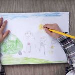 Child drawing a colorful outdoor scene with figures and a sun