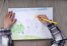 Child drawing a colorful outdoor scene with figures and a sun