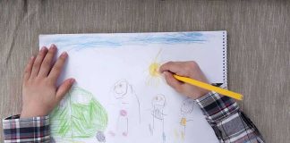 Child drawing a colorful outdoor scene with figures and a sun