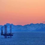An oil rig in the ocean with a backdrop of mountains during sunset