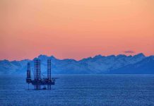An oil rig in the ocean with a backdrop of mountains during sunset