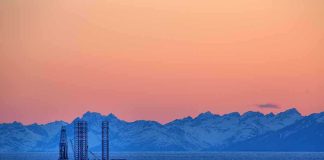 An oil rig in the ocean with a backdrop of mountains during sunset