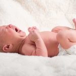 A newborn baby lying on a soft blanket, crying with a distressed expression