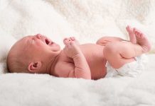 A newborn baby lying on a soft blanket, crying with a distressed expression