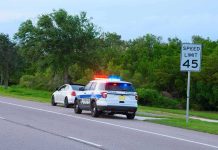 Police car with flashing lights pulling over a white vehicle beside a speed limit sign