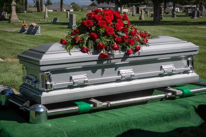 Silver casket with rose bouquet in a cemetery.
