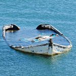 Half-submerged, weathered, abandoned boat floating on calm water.