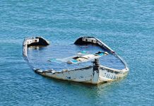 Half-submerged, weathered, abandoned boat floating on calm water.