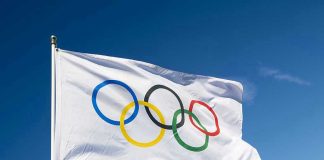 Olympian Sparks TRANS Sports Firestorm Olympic flag waving against clear blue sky.