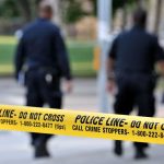 Police officers walking past caution tape at a crime scene