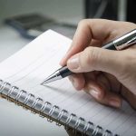 A hand holding a pen above a blank notebook page