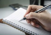 A hand holding a pen above a blank notebook page