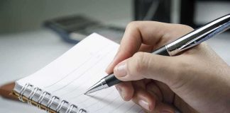 A hand holding a pen above a blank notebook page