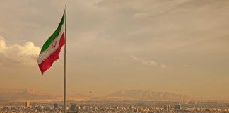 Trump’s Iran Blitz—Military Decimated in Weeks Iranian flag waving over a city skyline with mountains in the background