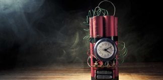 A stick of dynamite with a clock timer and wires, set against a dark smoky background