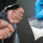 Person handcuffed, police holding bag of white substance.