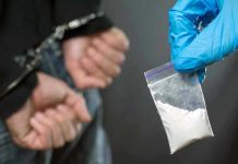Person handcuffed, police holding bag of white substance.