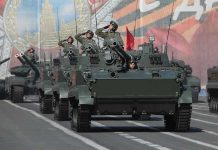 Tanks with military personnel in street parade formation.