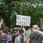 Crowd holds No More Mandates sign at protest.