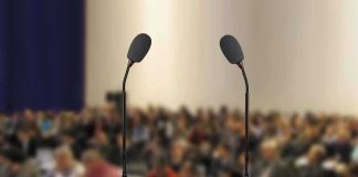 100-Year-Old Warning Haunts Modern Economics A wooden podium with two microphones in front of a blurred audience