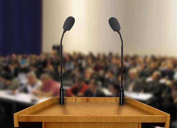 shutterstock_83211922 A wooden podium with two microphones in front of a blurred audience