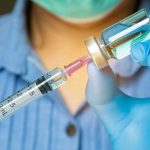 Gloved hands preparing a syringe with vaccine vial.