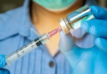 Gloved hands preparing a syringe with vaccine vial.