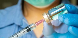 Gloved hands preparing a syringe with vaccine vial.