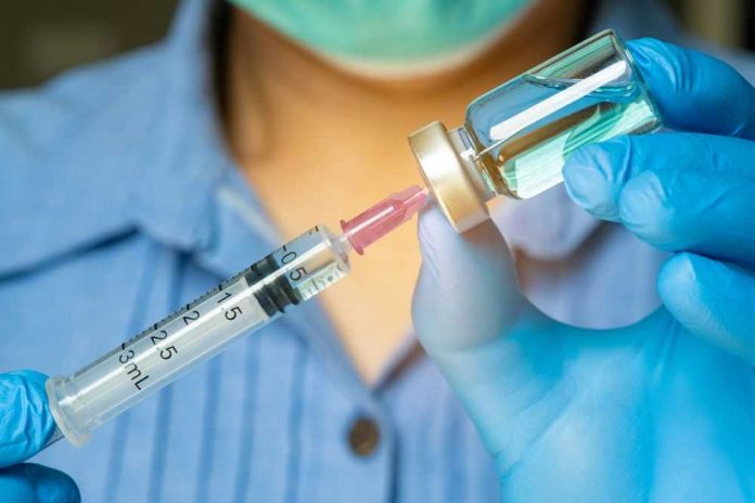 Gloved hands preparing a syringe with vaccine vial.