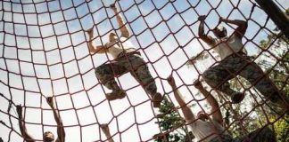 People climbing a red rope net outdoors.