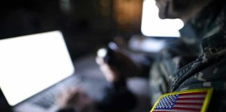 Trump Vows 20-To-1 Payback Soldier using laptop with US flag patch visible.