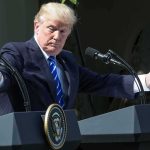Power Play: Trump Dangles Iran Meeting man at podiums with arms outstretched during outdoor press event
