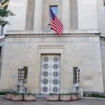 DOJ Goes Nuclear After D.C. Ambush Facade of a government building featuring the American flag and decorative entrance