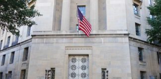 DOJ Goes Nuclear After D.C. Ambush Facade of a government building featuring the American flag and decorative entrance