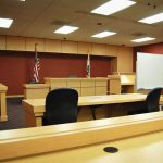FBI Flags Noncitizen Ballots Interior view of an empty courtroom with wooden furniture and American flags