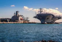 Aircraft carrier and support ships docked at a naval harbor