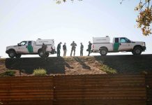 Border patrol agents stand between two trucks on a ridge