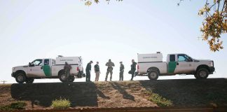 Border patrol agents stand between two trucks on a ridge