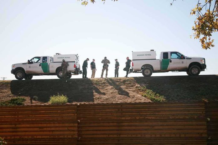 Border patrol agents stand between two trucks on a ridge