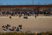 Crowd of people gathered along a tall border fence