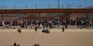 Crowd of people gathered along a tall border fence