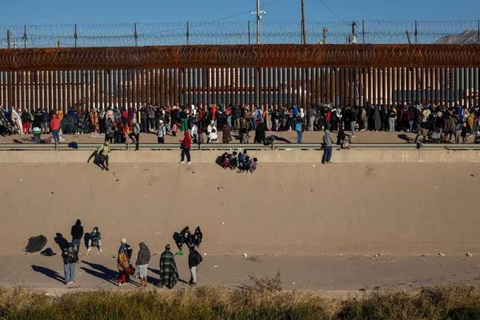 shutterstock_2257563879 Crowd of people gathered along a tall border fence