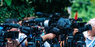TV news cameras crowding together at an outdoor event
