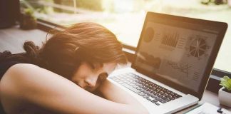Woman resting her head on desk beside an open laptop