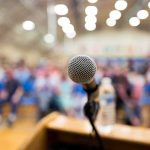 Streamer Practically SWOONS Over Trump Insult microphone on a podium facing a blurred audience
