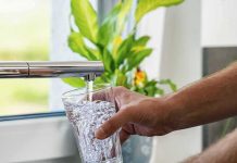 Hand filling a glass with water from a kitchen faucet