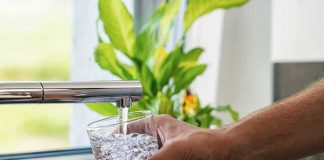 Hand filling a glass with water from a kitchen faucet