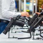 DOJ Quietly Guts Under‑21 Handgun Ban Handguns displayed on stands at a trade show counter