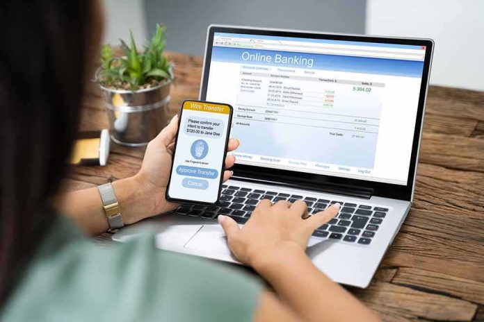 Person using smartphone to approve bank transfer beside laptop with online banking